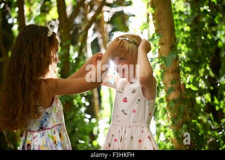 Two girls putting on tiaras in sunlit forest Stock Photo