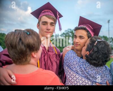 Two young men hugging family at graduation ceremony Stock Photo