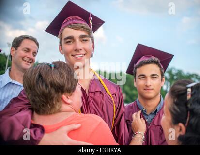 Two young men hugging family at graduation ceremony Stock Photo