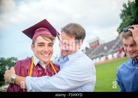 Young man being hugged by father at graduation ceremony Stock Photo