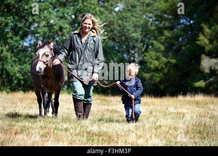 Mother and son walking pony in field Stock Photo