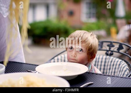 Boy sitting at garden table waiting for spaghetti to be served Stock Photo
