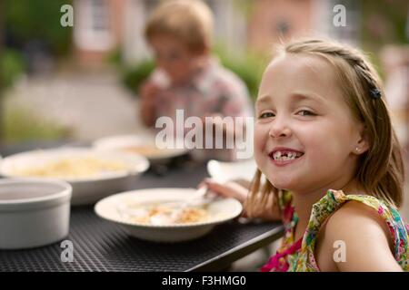 Girl dining at garden table, looking over shoulder smiling at camera Stock Photo