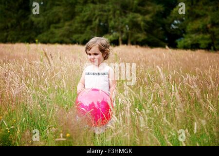 Girl in tall grass holding red balloon looking away Stock Photo