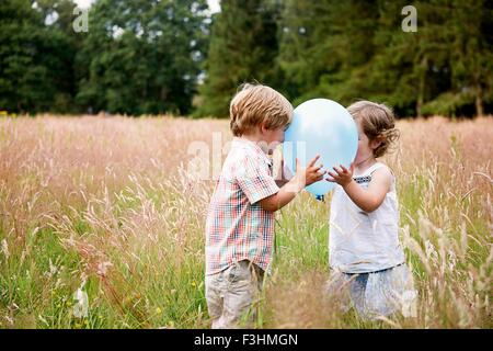 Brother and sister in tall grass face to face playing with balloon Stock Photo