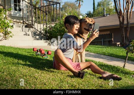 Boy posing for smartphone selfie with dog in garden Stock Photo