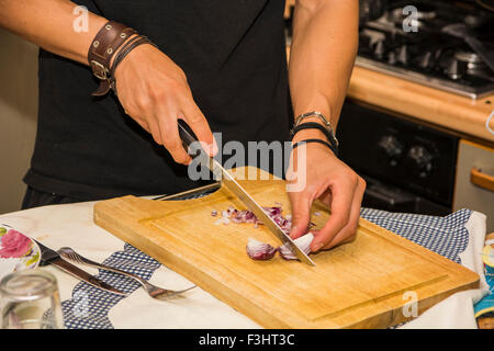 Close up of Young Man's hands Chopping Red Onion with Sharp Knife in Kitchen - Close Up of Man Cooking in Kitchen of First Apart Stock Photo