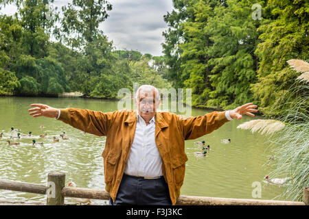 senior with suede jacket and white shirt in a green park with open arms Stock Photo