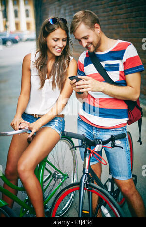 Young couple on bicycles using cellphone outdoors Stock Photo