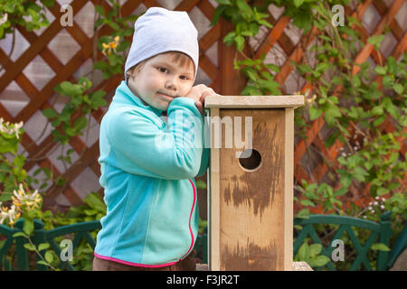 Cute smiling Caucasian blond girl stands near new handmade nesting box Stock Photo