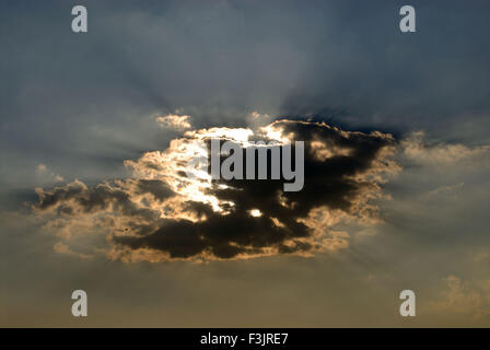 Sun behind black grey white clouds with silver lining Stock Photo