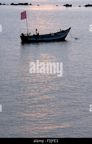 Sparkling sea water at sunset with small empty country fishing boat at Malvan beach ; Arabian sea Sindhudurg maharashtra india Stock Photo