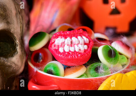 closeup of a red bowl with different Halloween candies, and some scary ornaments, such as a skull or a carved pumpkin Stock Photo