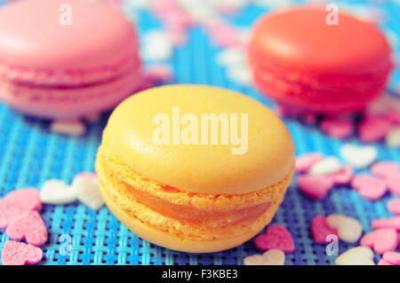 closeup some appetizing macarons with different colors and flavors on a blue tablemat with heart-shaped sprinkles Stock Photo