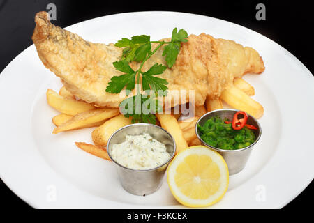 Fish and Chips, a traditional English meal served with Sour cream, mushed peas, coriander  and Lemon Stock Photo