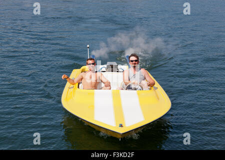 Two smiling men in a yellow and white speedboat having fun in the sunshine. Stock Photo