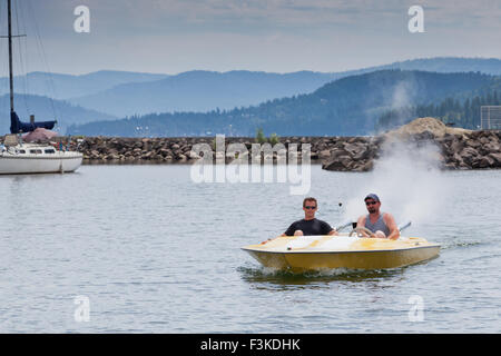 Two me in a small speedboat going slow through a now wake zone in a marina. Stock Photo