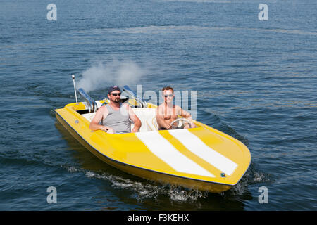 Two men in a yellow and white speedboat having fun in the sunshine. Stock Photo