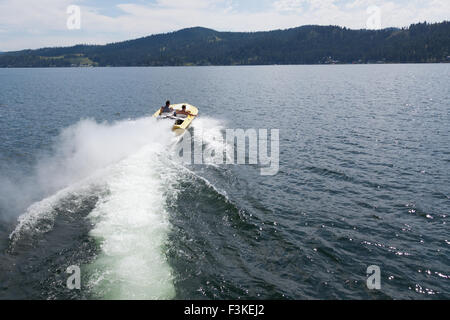 Two men in a yellow speedboat heading out into a lake on a sunny summer day. Stock Photo