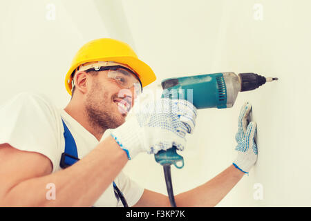 smiling builder in hardhat drilling wall indoors Stock Photo