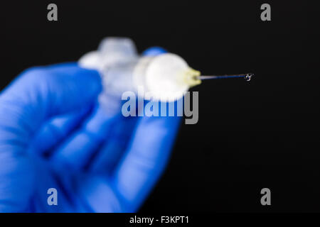 A hand in a blue medical glove is holding a syringe with a hypodermic needle and a drop of medicine for medical use, displayed o Stock Photo