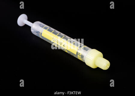 A yellow pharmaceutical phial for medical use, displayed on a black table Stock Photo