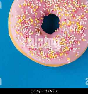 donut with pink frosting and sprinkles on turquoise background Stock Photo