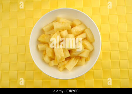 White bowl of pineapple pieces against a yellow woven textured background Stock Photo