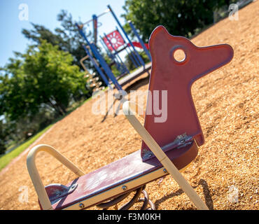 Red rocking horse in summer with children's jungle gym and park in the background Stock Photo