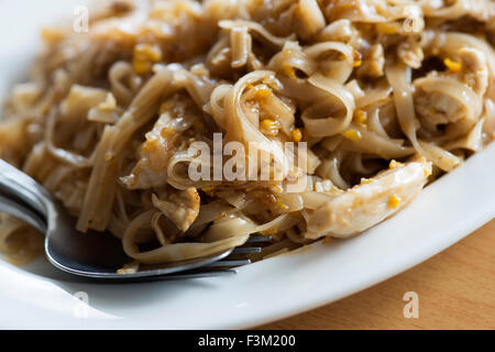 Closeup of chicken pad thai on a white plate with a fork and spoon Stock Photo