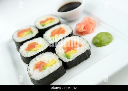 Freshly cut salmon sushi rolls on a white plate with soy sauce, wasabi and pickled ginger Stock Photo