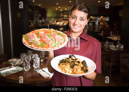 Waitress holding Parma pizza and Seafood Linguine, Strada, Italian chain restaurant, Covent Garden, London, England, UK Stock Photo
