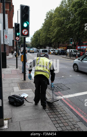 Man from water company pulling up drain covers in London street Stock Photo