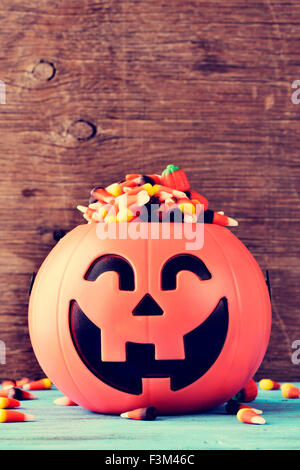 a carved pumpkin full of different halloween candies on a rustic blue wooden surface Stock Photo