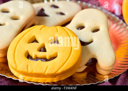 closeup of a golden tray with a pumpkin-shaped cookie and some other ghost-shaped cookies Stock Photo
