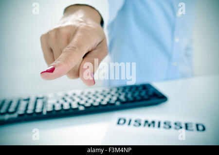 closeup of a businesswoman sitting at her desk, with a document with the text dismissed on it, pointing with her finger the way Stock Photo