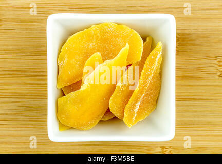 Dehydrated dried mango in white bowl on wooden background Stock Photo
