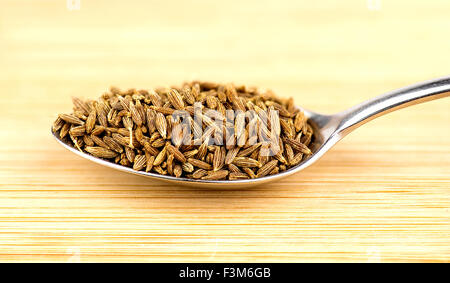 Spoonful of cumin seeds against wooden background Stock Photo