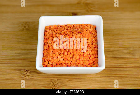 Macro of red split lentils in white bowl on wooden board