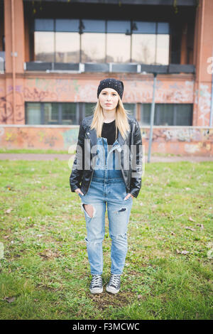 young beautiful blonde straight hair woman posing in the city, hands in pocket, looking in camera, pensive - thoughtful, thinking future concept Stock Photo