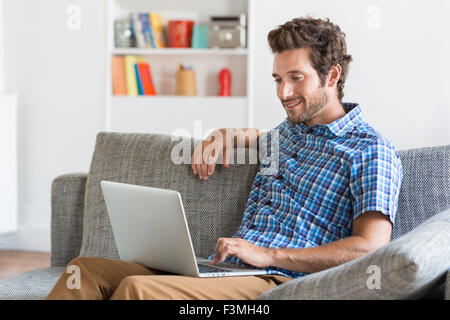 Mid adult man using laptop sitting on a couch in moder white apartment. Stock Photo