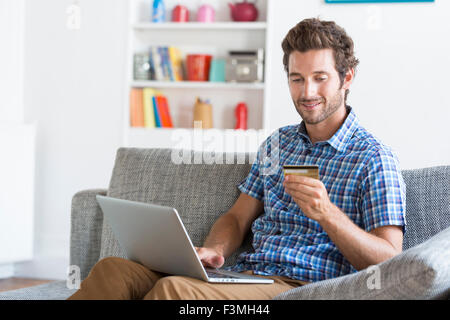 Mid adult man shopping using laptop and credit card in modern apartment. Ecommerce Stock Photo