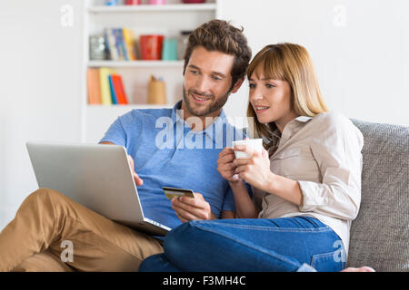 Mid adult couple shopping using laptop and credit card in modern apartment. Online Shooping Stock Photo