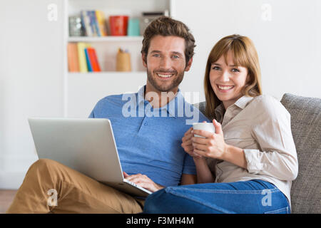Portrait of young couple surfing on internet with laptop. Modern white apartment in background. Looking at camera Stock Photo