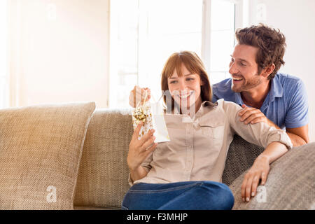Man offering a gift to his wife for birthday. Gift, sofa, home, girlfriend, couple Stock Photo