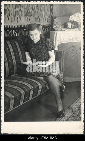 Vintage photo. Woman sitting on the couch is reading a book. Germany, circa 1946 Stock Photo