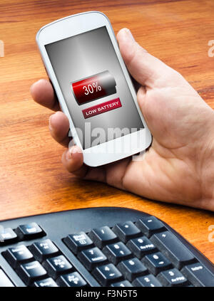A man holding phone on the table with a low battery icon in the screen, soft focus Stock Photo