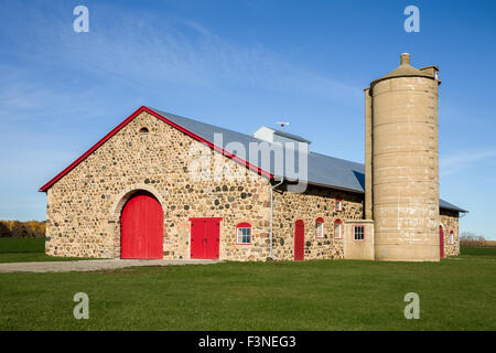 Retro field stone barn with bright red doors set against a blue sky.  Vibrant colors and texture. Stock Photo