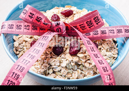 Diet healthy food weight loss concept. Oatmeal in blue bowl with measuring tape around on kitchen table Stock Photo