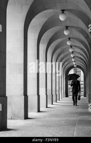 Man in suit walking to work with umbrella and suitcase through archways of Manchester Town Hall, England Stock Photo